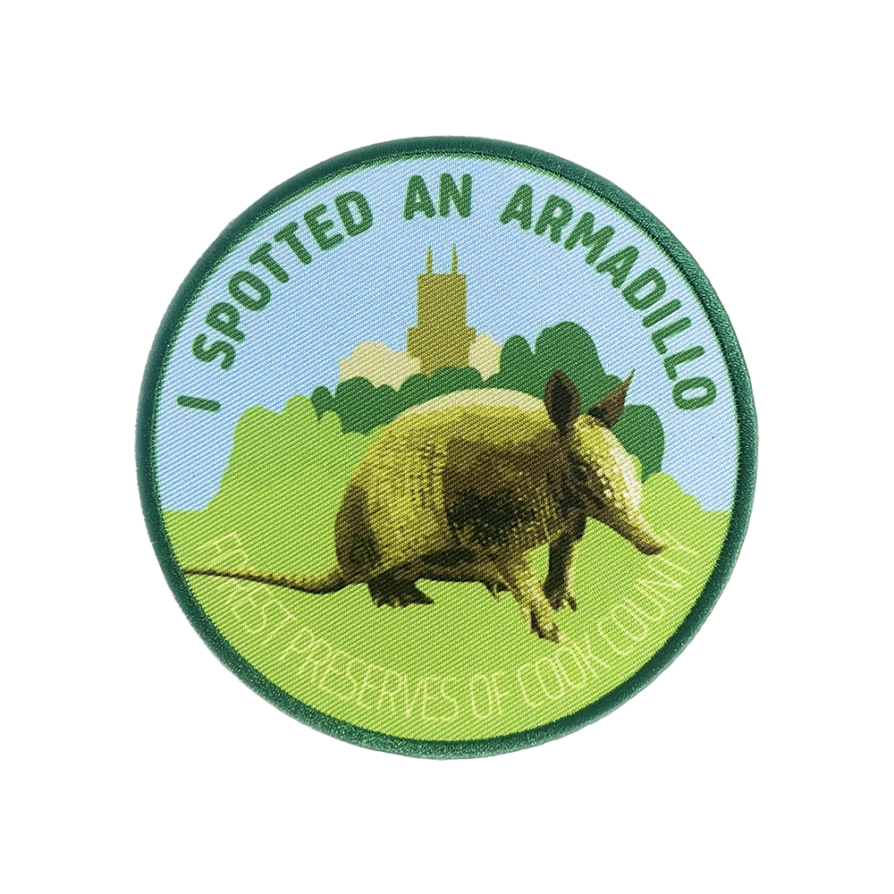 Round patch illustration showing an armadillo walking through vegetation in front of the Chicago Skyline, labeled “I Spotted an Armadillo – Forest Preserves of Cook County.”
