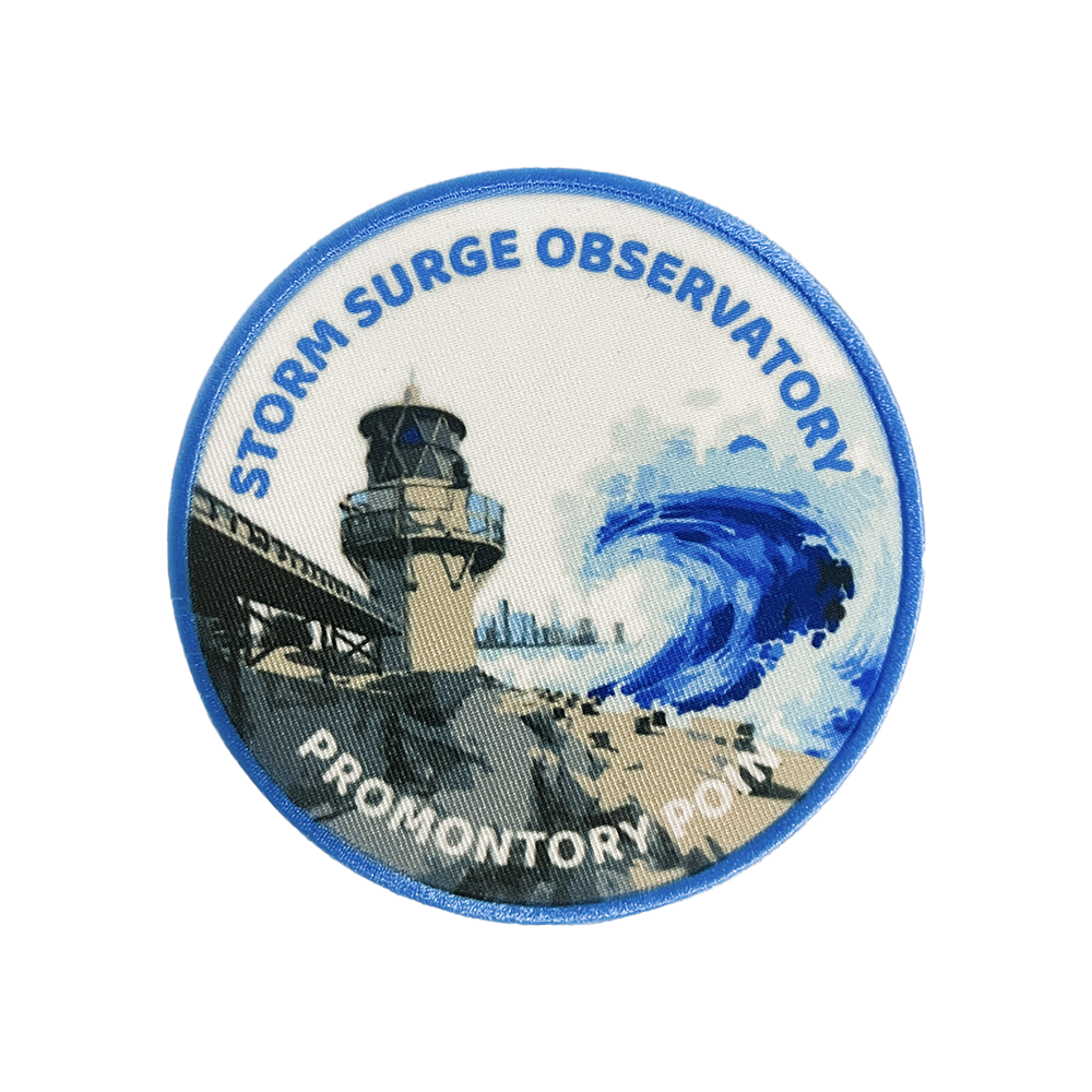 Rectangular patch featuring satellites powering a skillet cooking sausages underneath sunlight, with a  cooked sausage on a fork in the foreground. Text reads “Windy City Solar Cook-Off.”